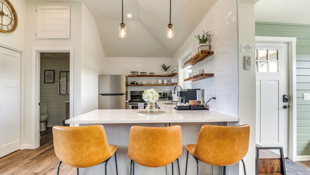 Una cucina moderna con isola centrale, luci a sospensione e vista sul bagno adiacente.