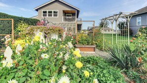 Una casa a due piani con un balcone, immersa in un giardino curato e ricco di fiori e piante.