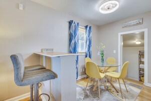 Una zona de comedor con barra, un taburete de bar y una mesa con cuatro sillas.
