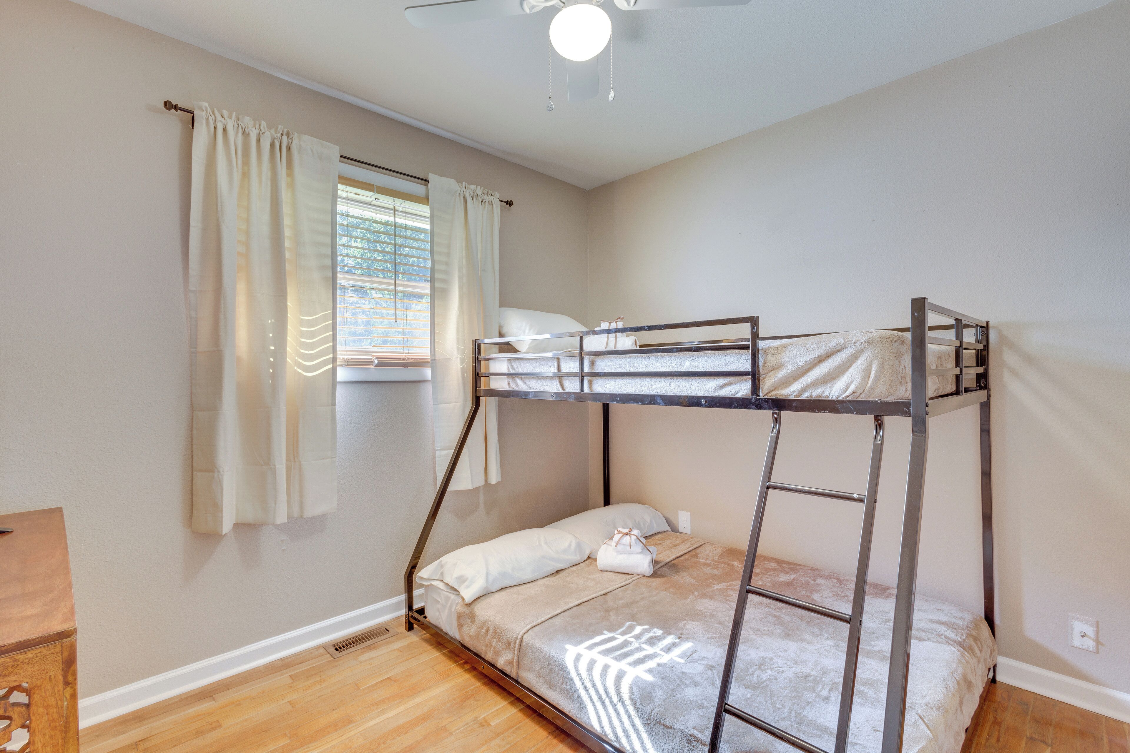 A bunk bed room with a window, curtains, and a ceiling fan.