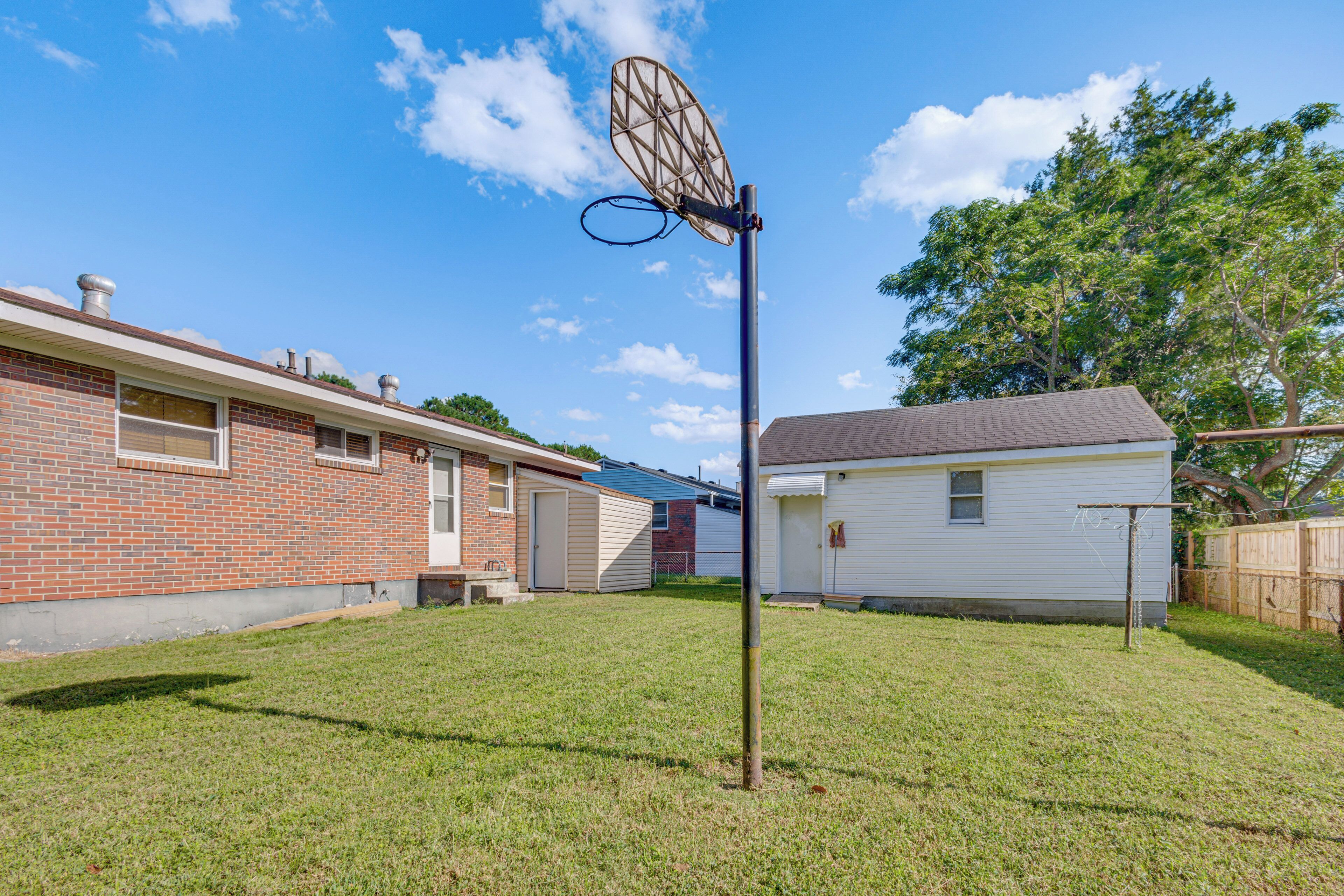 A backyard with a basketball hoop, a brick house, and a white house.