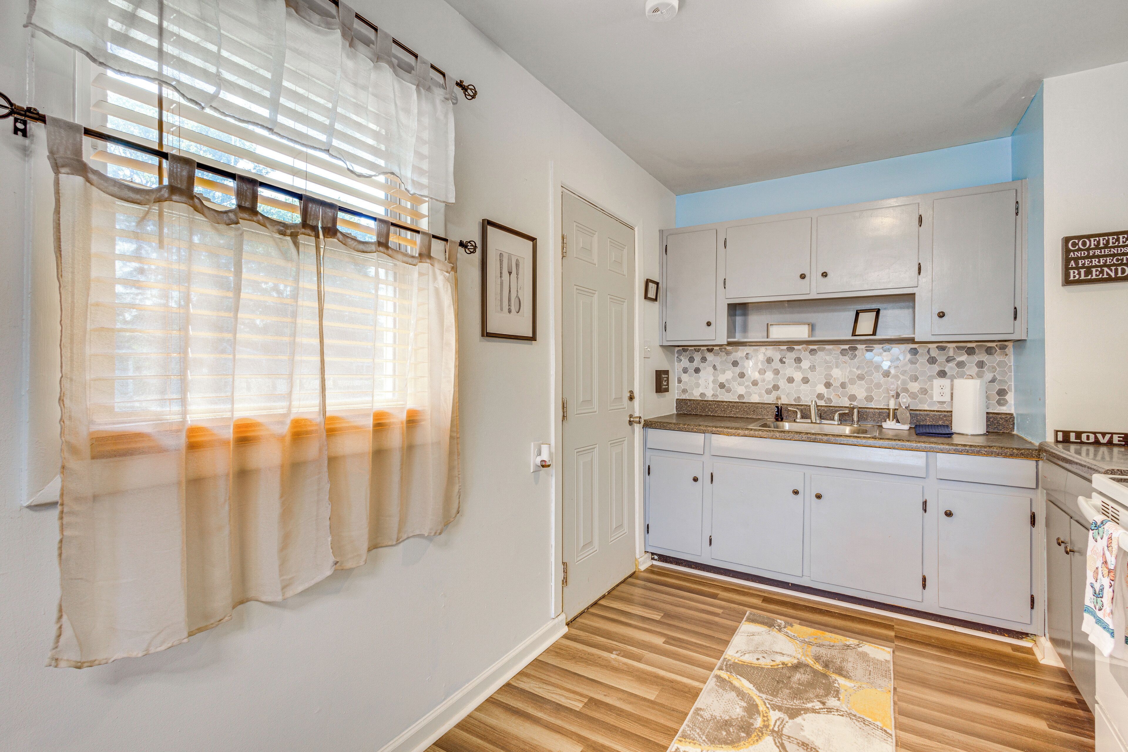 Una cocina con armarios azul claro, piso de madera y ventana con cortinas de gasa.