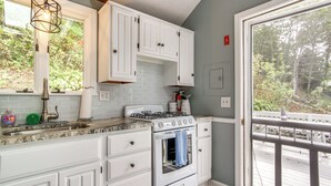 A kitchen with white cabinets, a gas stove, and a large window. - Swim & Fish On-site! Waterfront Cape Cod Cottage (Mashpee)