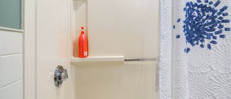 A bathroom with a white bathtub, a red bottle on a shelf, and a shower curtain with a blue pattern.