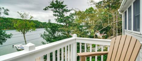 A wooden deck with a white railing overlooking a lake, surrounded by trees.