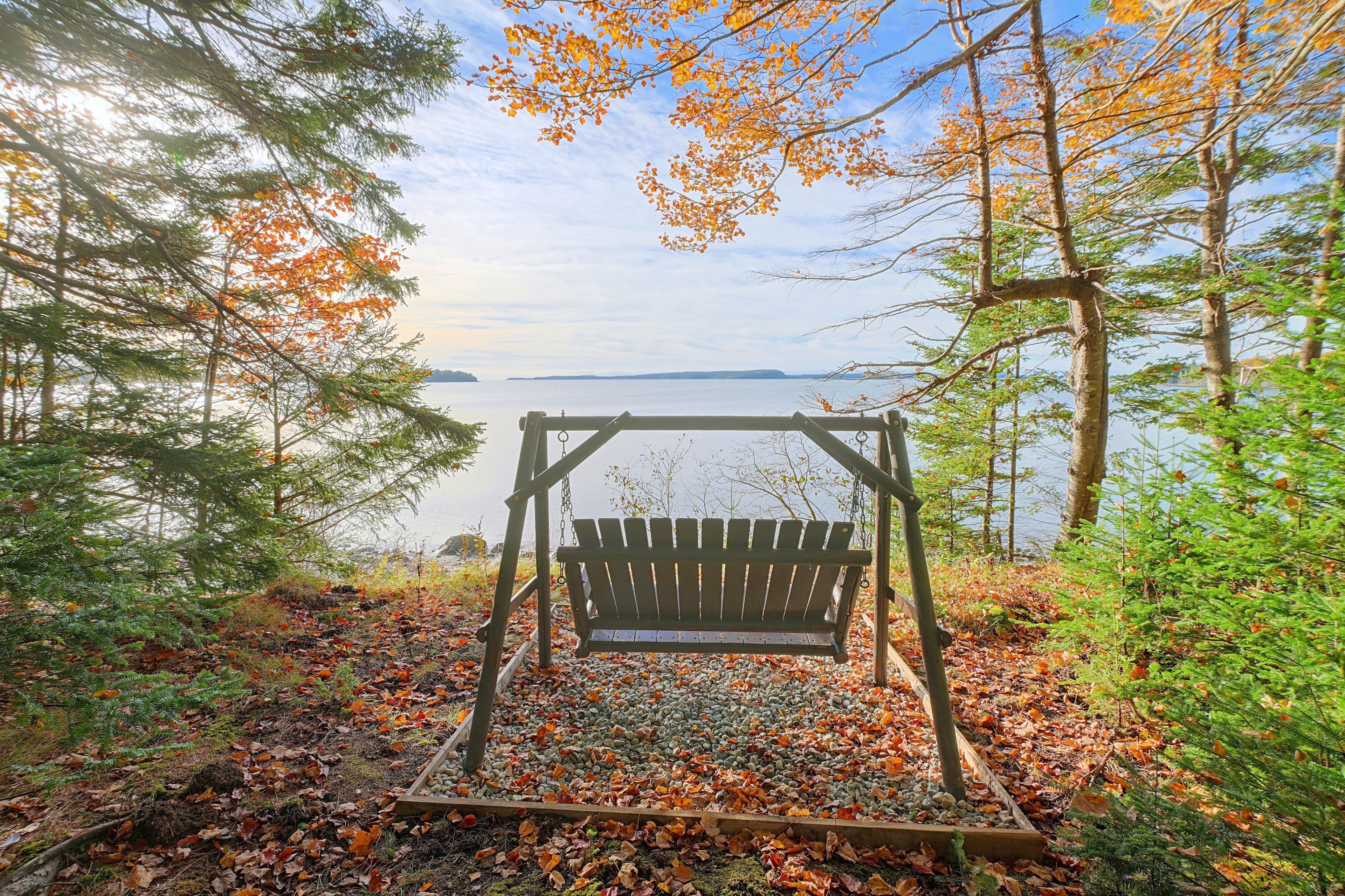 A wooden swing set in a forested area with a view of a lake.