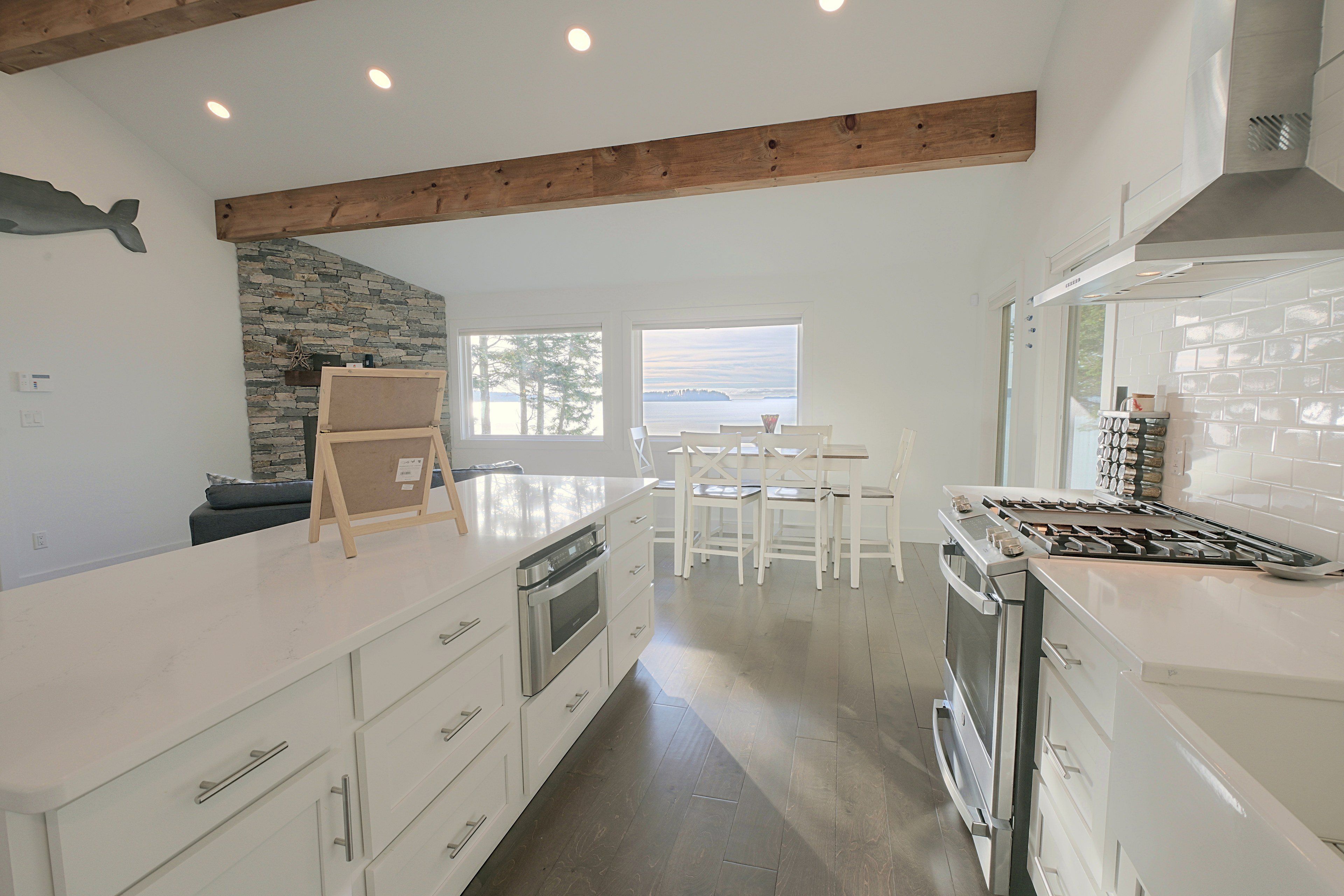 A modern kitchen with white cabinetry, a stone accent wall, and a view of the water.
