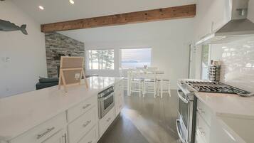 A modern kitchen with white cabinetry, a stone accent wall, and a view of the water.