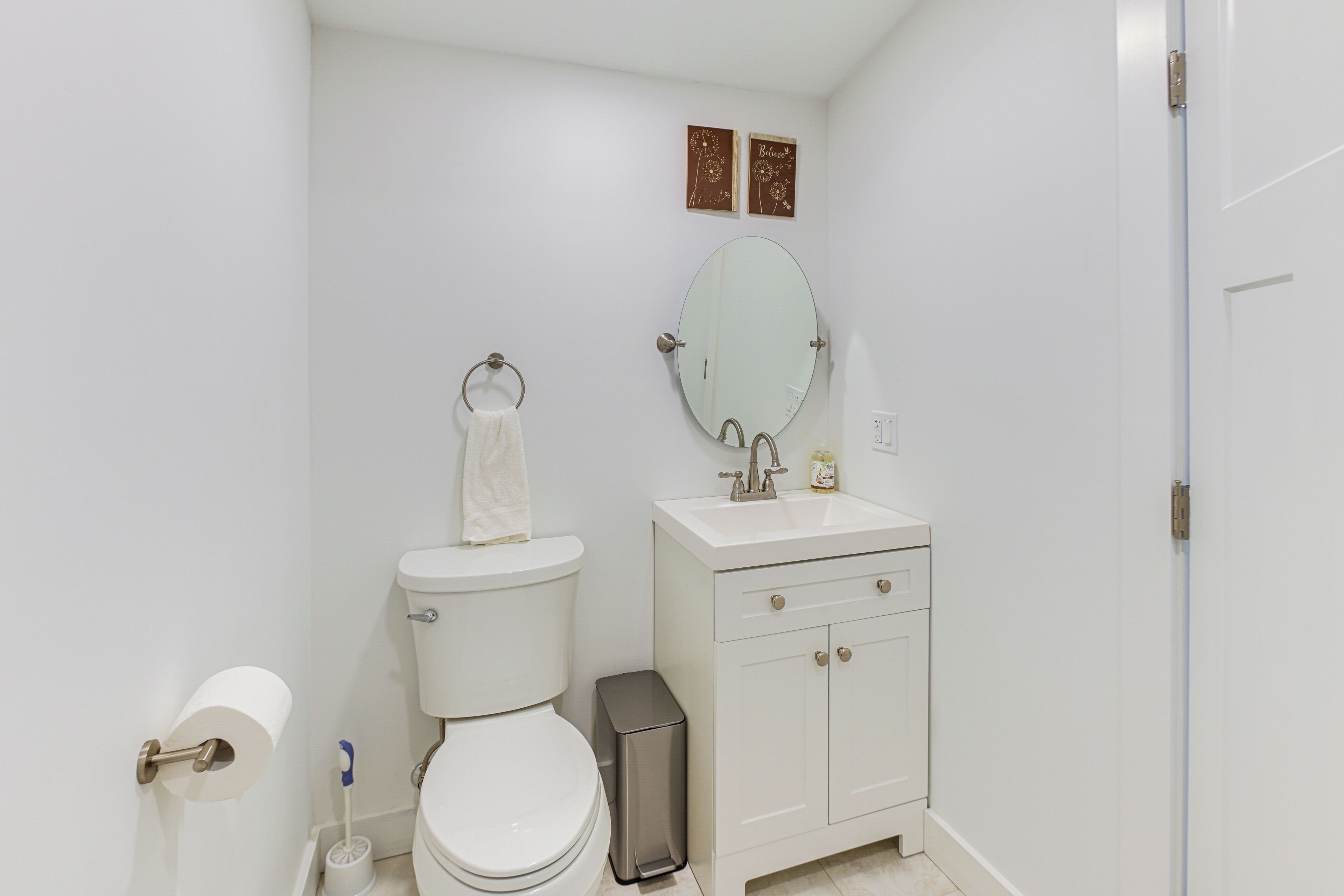 A bathroom with a toilet, sink, mirror, and toilet paper.