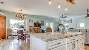 A spacious kitchen with a large island, wooden cabinets, and a dining area with patterned chairs. - Waterfront Gulf Coast Home w/ Outdoor Oasis! (Gautier)
