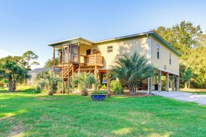 A two-story house with a covered porch, a wooden staircase, and a front yard with palm trees.