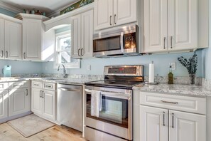 Una cocina moderna con armarios blancos, electrodomésticos de acero inoxidable, encimera de granito y una ventana que proporciona luz natural.