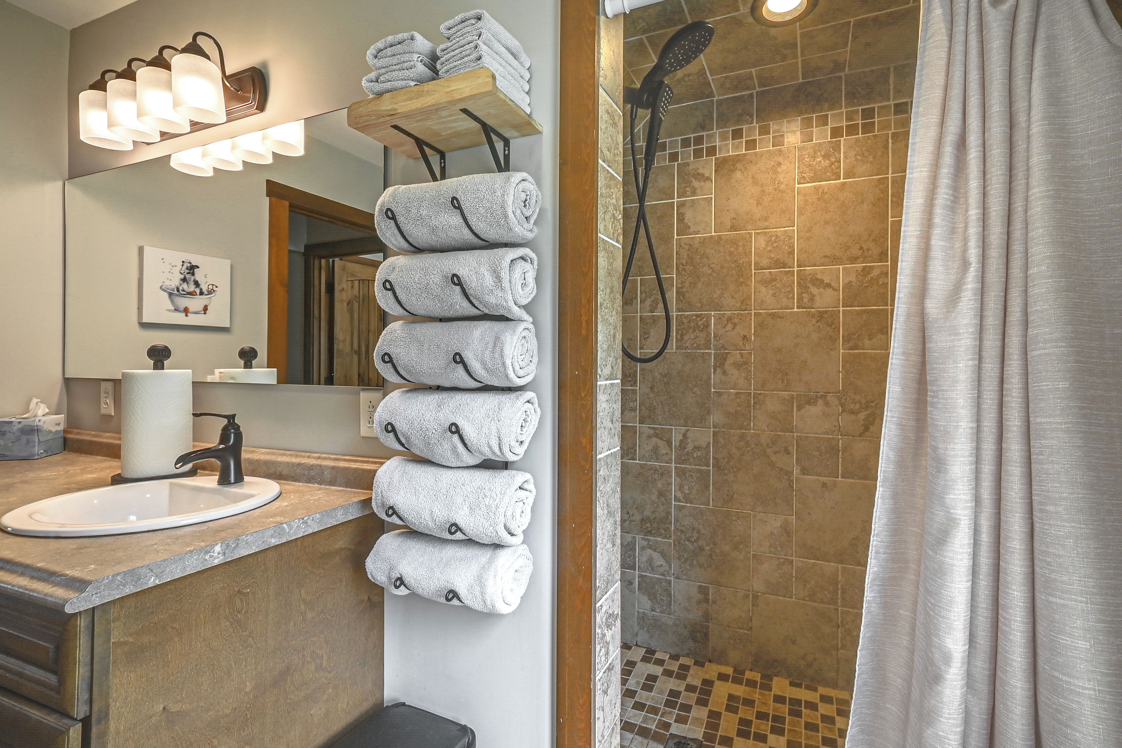 A bathroom with a sink, mirror, towel rack, shower, and tiled floor.
