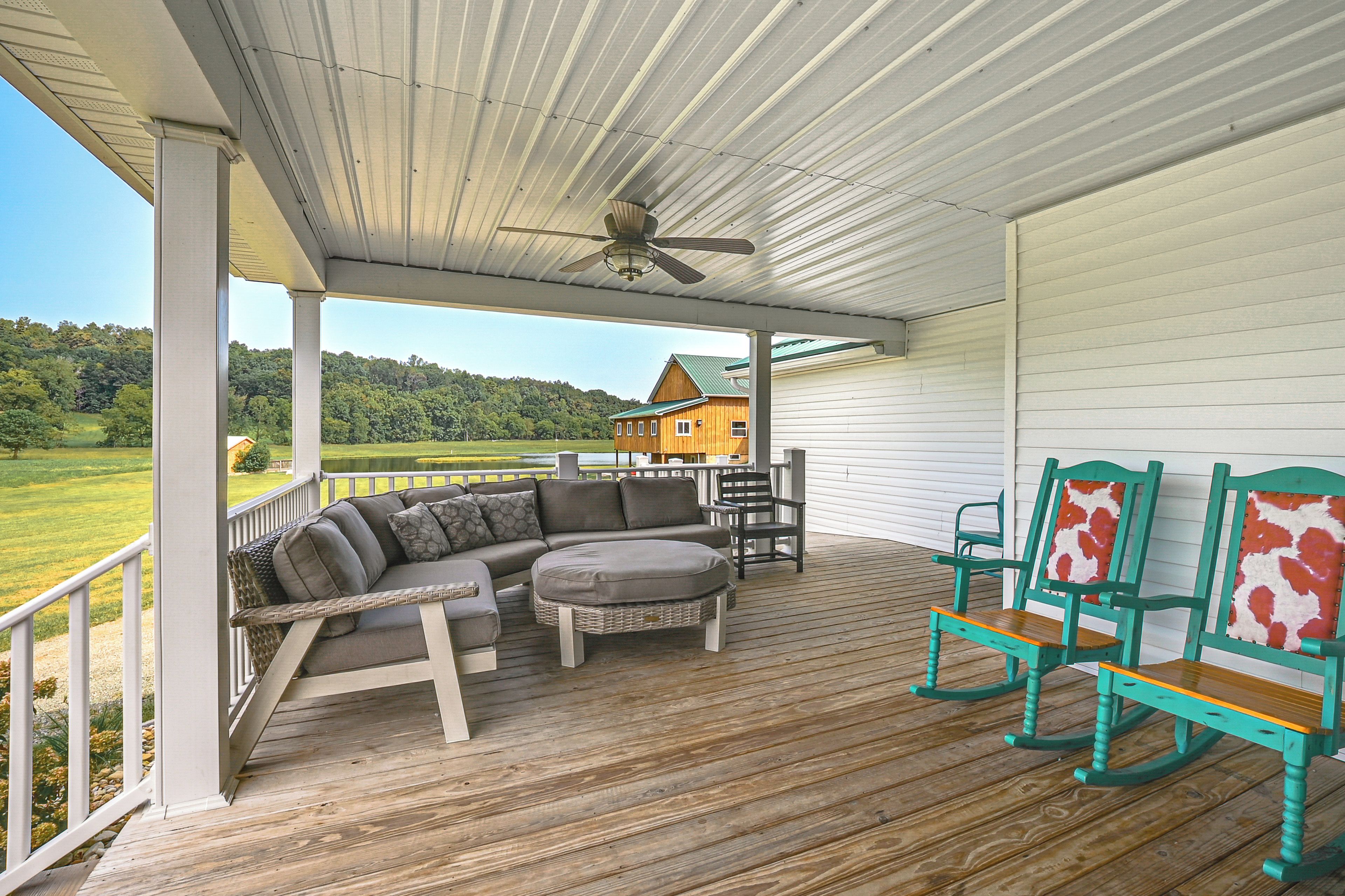 Une véranda couverte avec une terrasse en bois, du mobilier d’extérieur et une vue sur une maison et le paysage environnant.