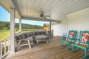 Une véranda couverte avec une terrasse en bois, du mobilier d’extérieur et une vue sur une maison et le paysage environnant.