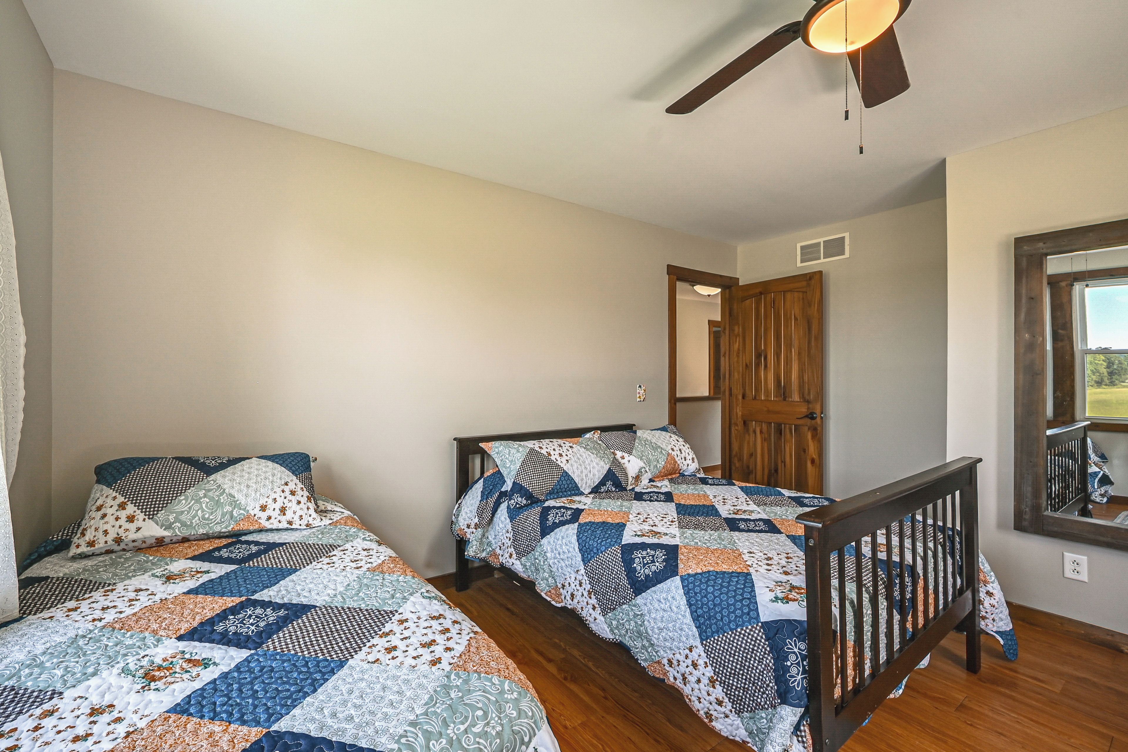 A bedroom with two beds, a ceiling fan, a wooden door, and a window.