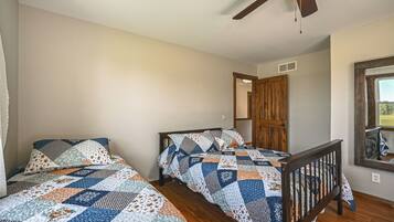 A bedroom with two beds, a ceiling fan, a wooden door, and a window.