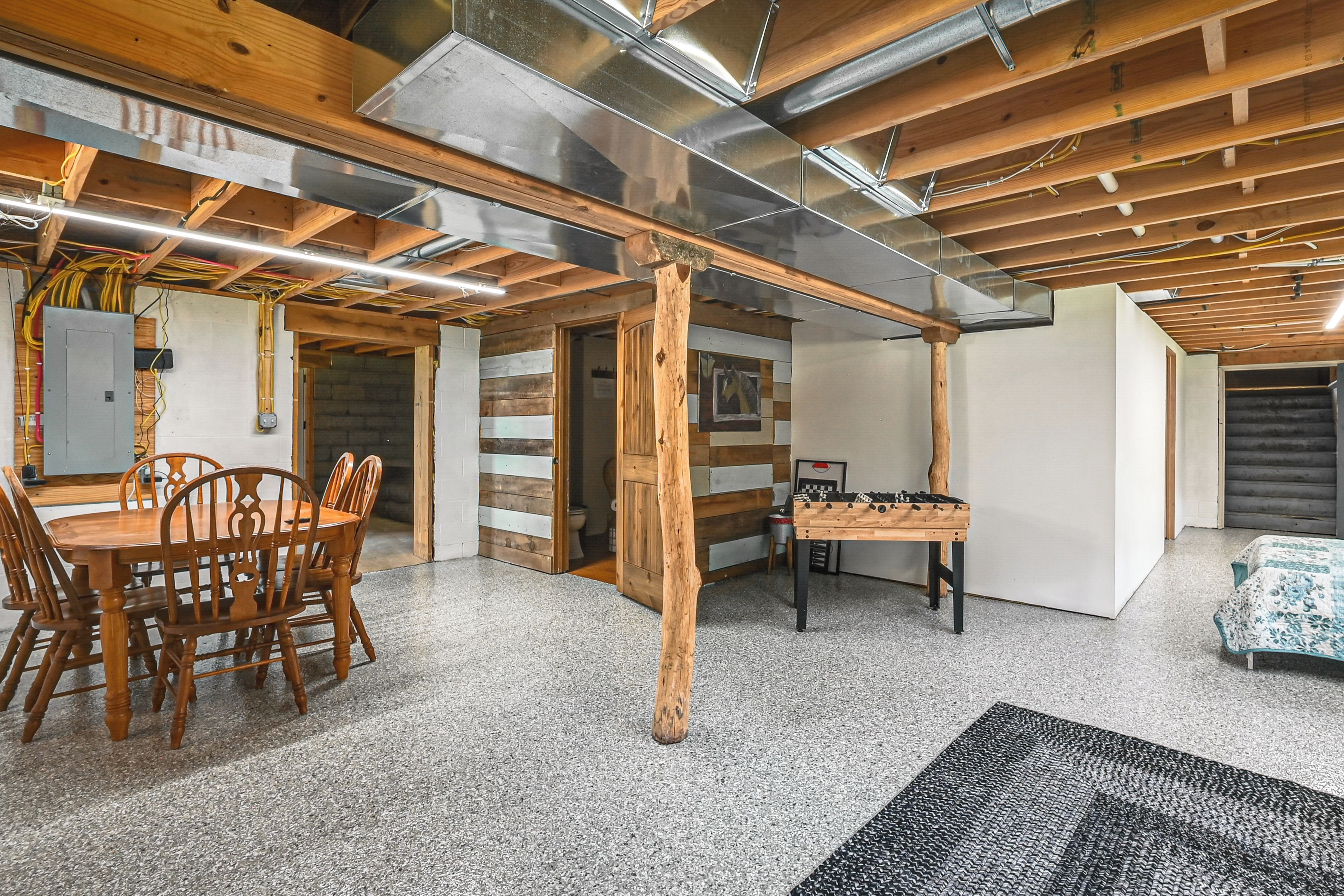 A room with a wooden dining table, chairs, a foosball table, and a staircase leading to an upper level.