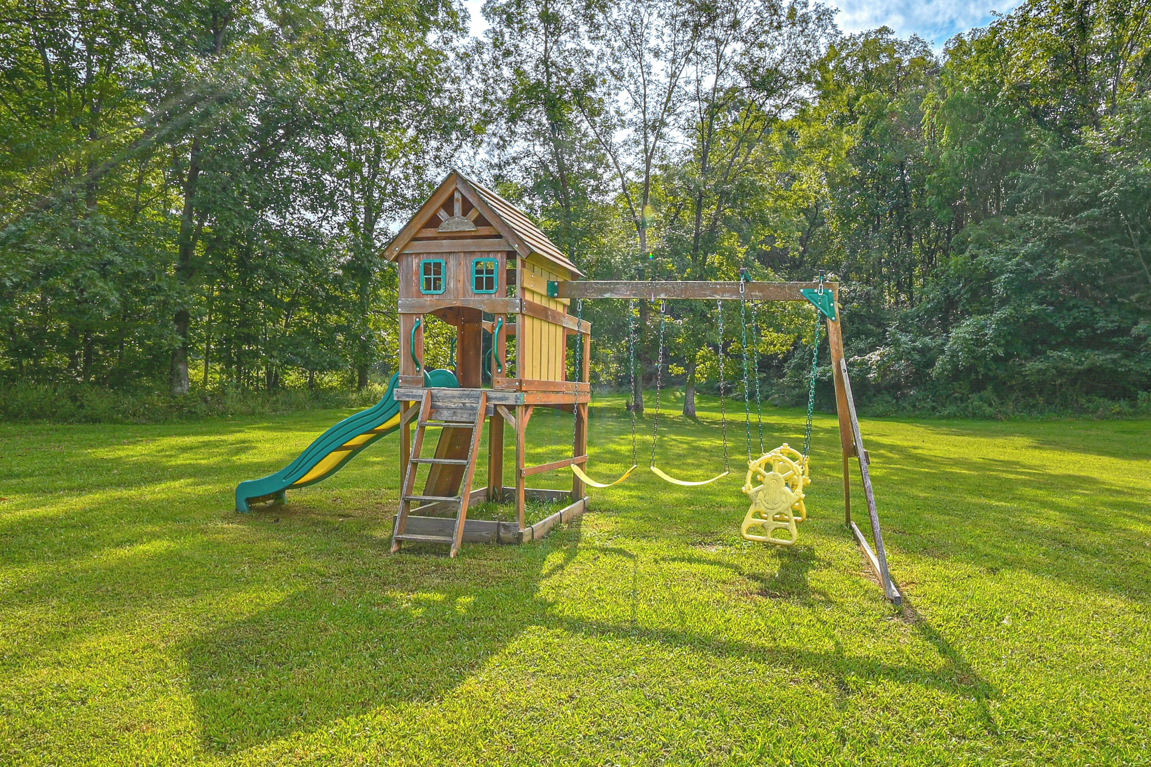Ein hölzernes Spielhaus mit Rutsche und Schaukeln in einem grünen Park.