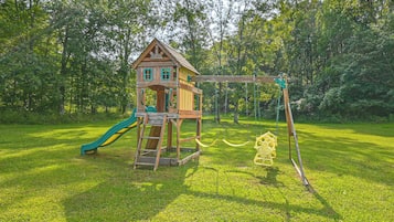 Una casita de juegos de madera con tobogán y columpios en un parque cubierto de césped.