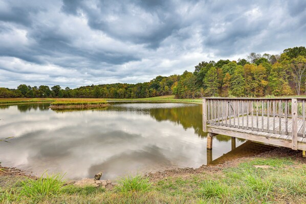 Un lac paisible avec une jetée en bois qui s’avance sur l’eau, entouré d’arbres et surplombé par un ciel nuageux.