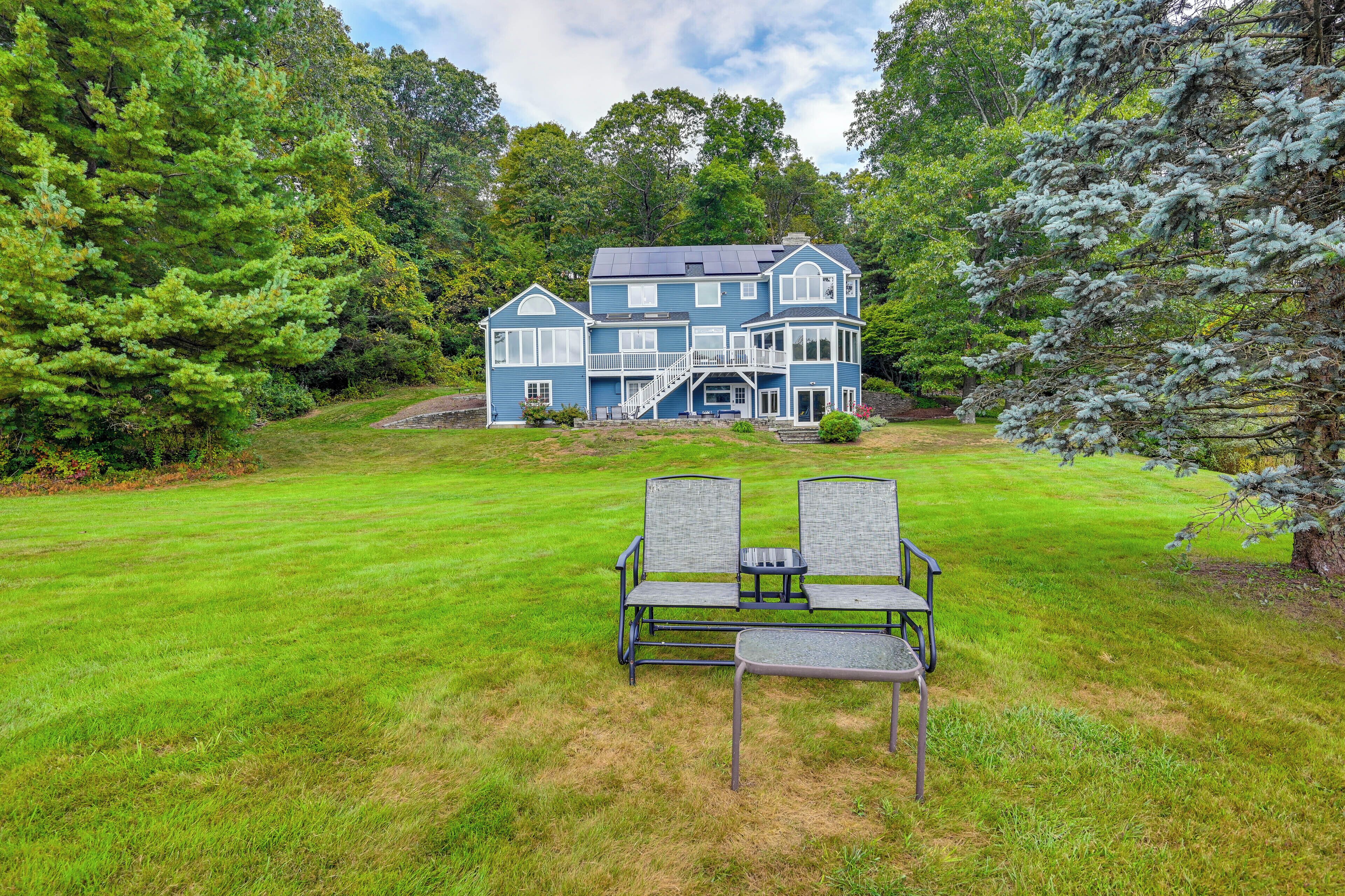 A two-story house with a large front lawn and a bench in the foreground.