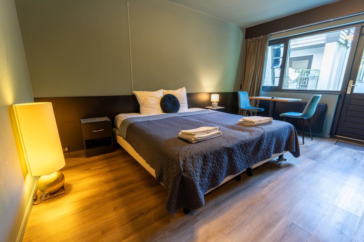 A hotel room with a bed, bedside tables, a desk, a chair, and a window with a view.