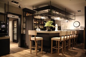 A modern bar area with a central island, bar stools, a clock, and shelves with bottles and glasses. - Hotel Zee Bergen (Bergen)