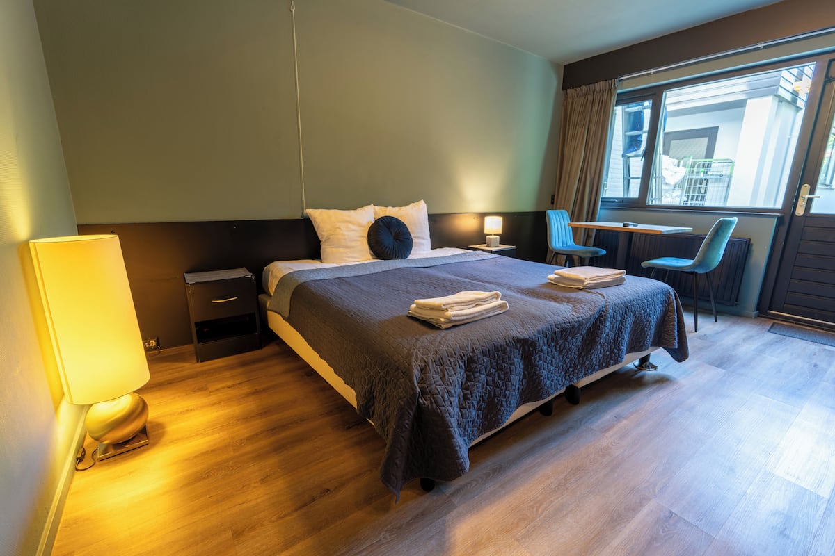 A hotel room with a large bed, bedside tables, a desk with a chair, and a window with curtains.