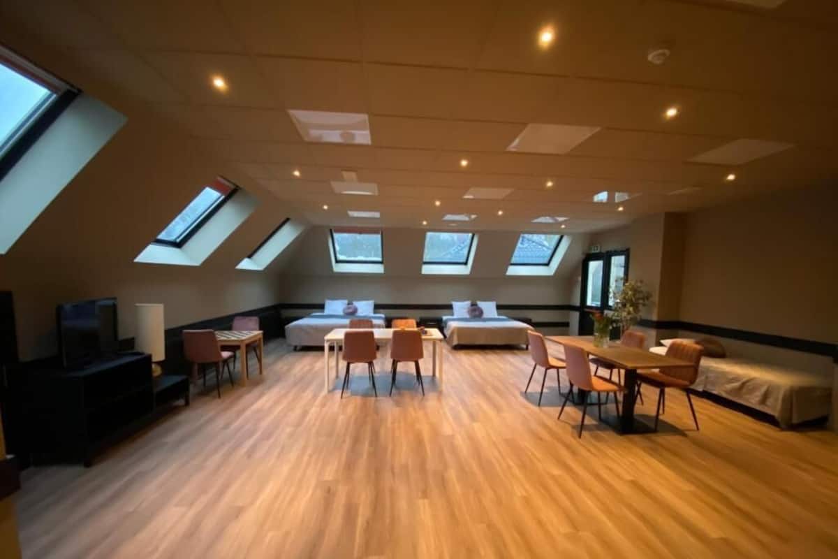 A spacious room with a high ceiling, skylights, a dining area, and a bed.