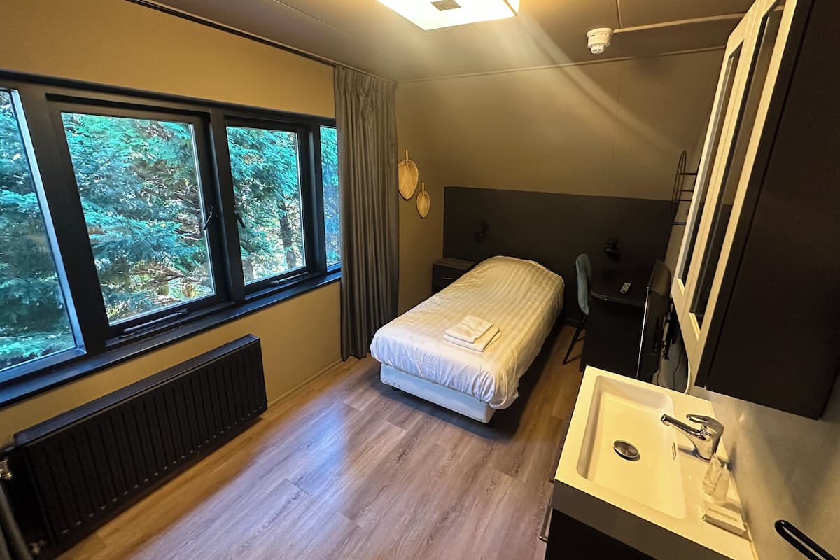 A modern bedroom with a bed, a desk, a chair, and a large window.