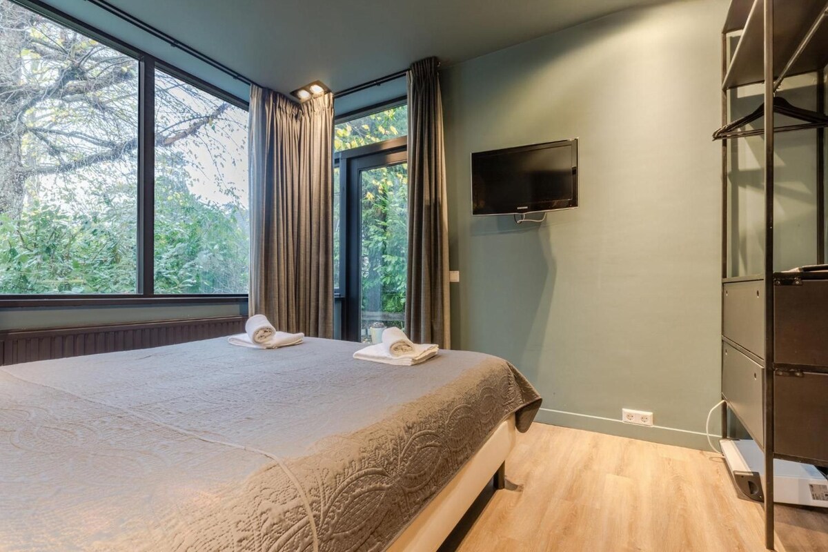 A hotel room with a large bed, a flat-screen TV mounted on the wall, and a window with curtains.