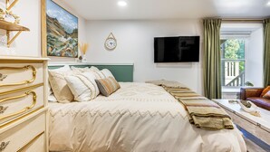 Ein Schlafzimmer mit Bett, Schminktisch, Fernseher und einem Fenster mit Vorhängen.