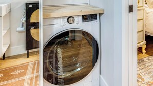 Eine Waschmaschine mit Frontlader, einer Bedienblende und einem Holzregal darüber.