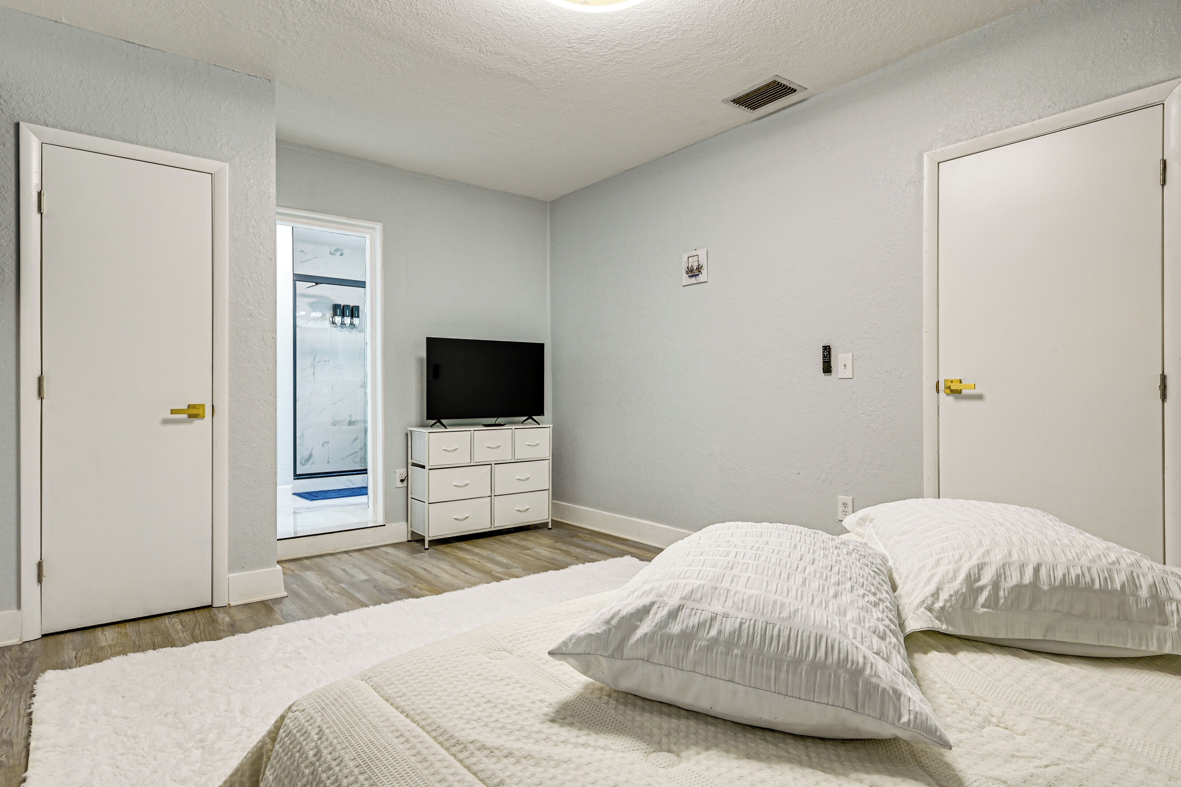 A bedroom with a bed, two pillows, a dresser, a TV, and a closet.