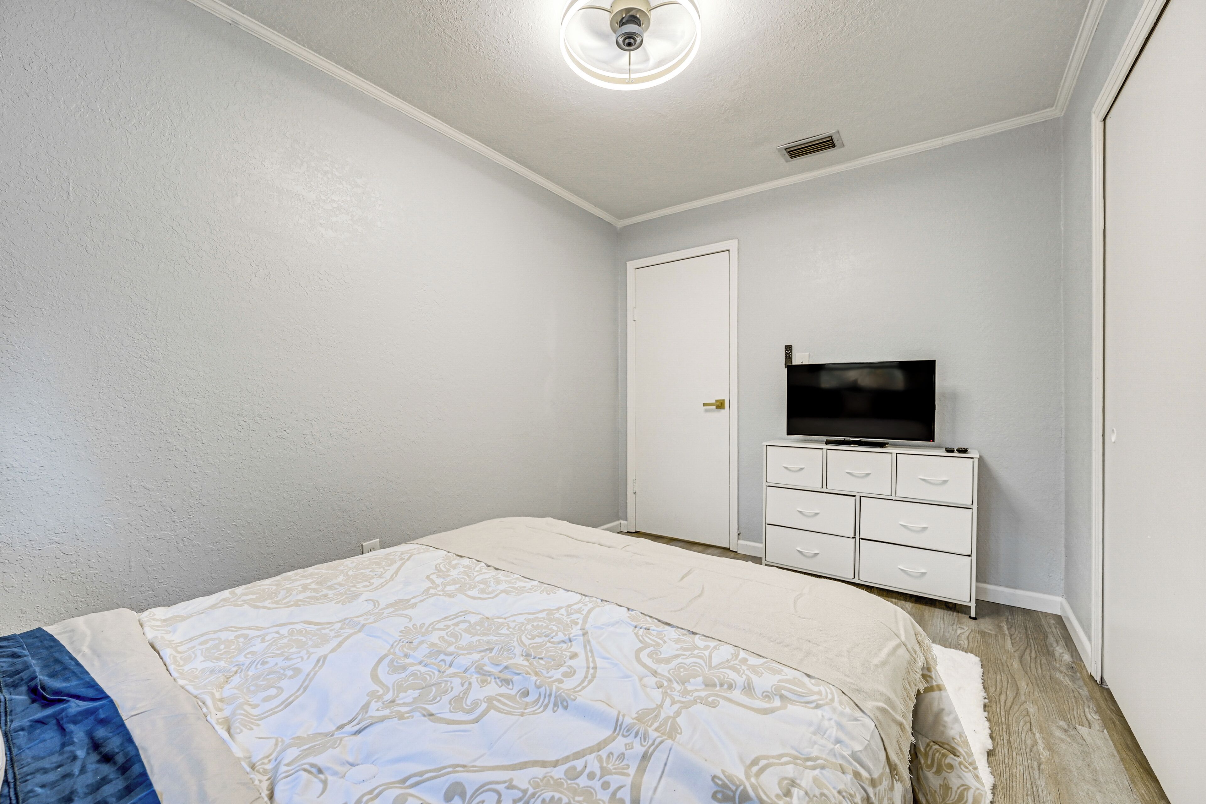 Ein Schlafzimmer mit Bett, Kommode, Fernseher und einer Tür.
