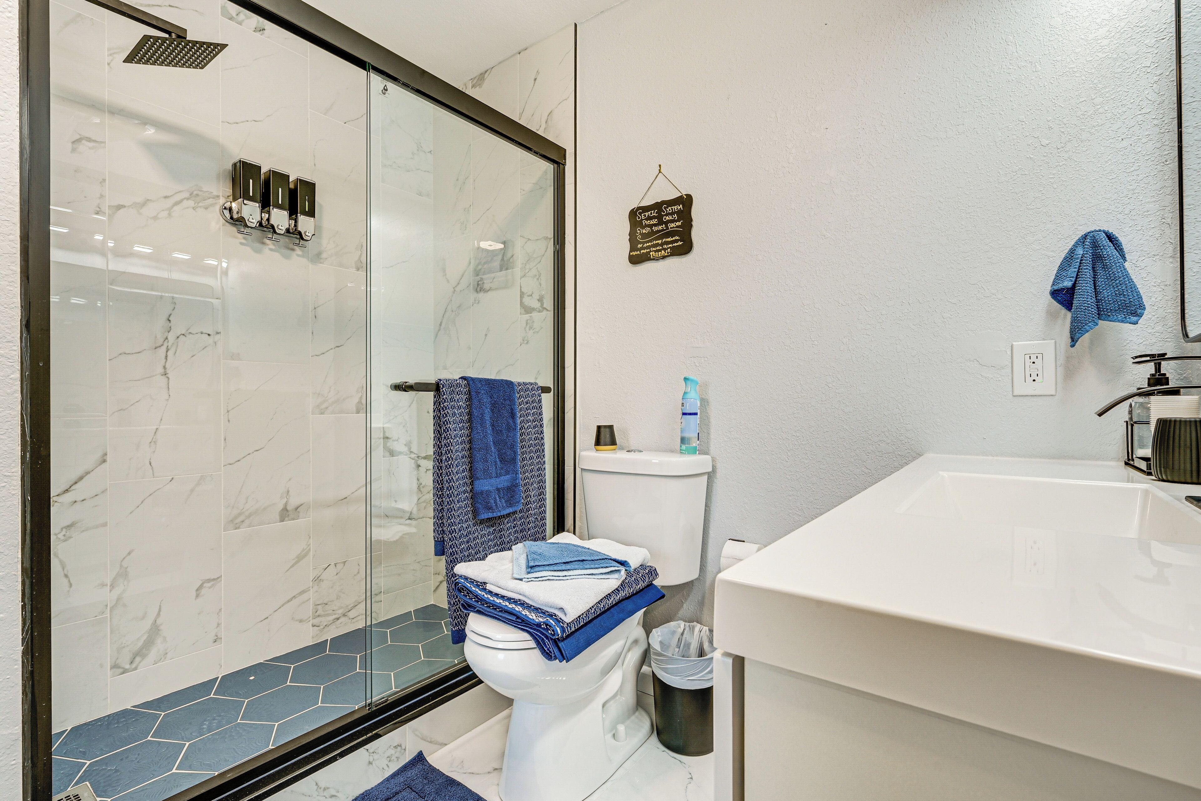 A bathroom with a glass shower enclosure, a toilet with a blue towel, and a sink with a blue towel.