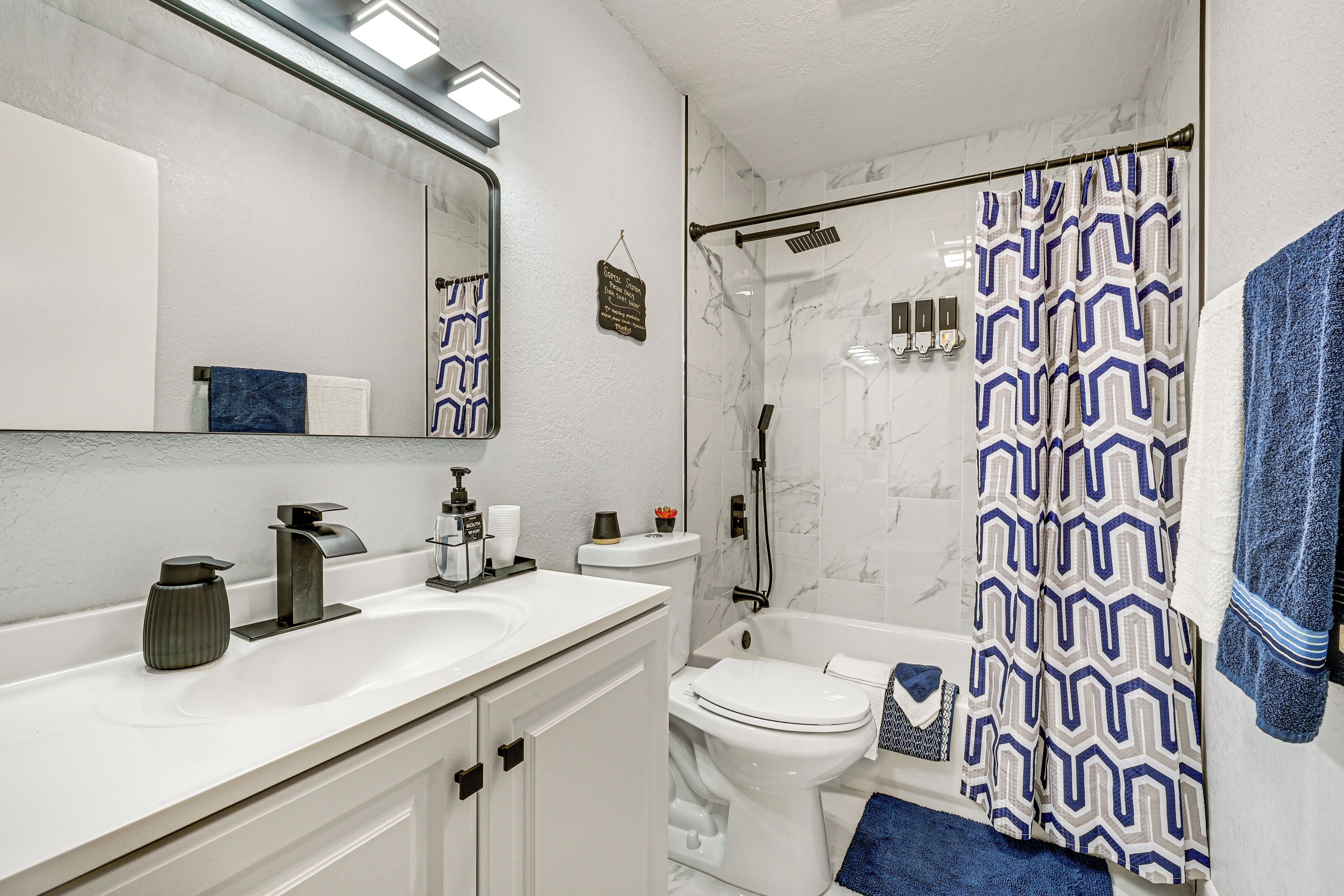 Un baño moderno con tocador blanco, un espejo grande, ducha con cortina estampada y un inodoro.
