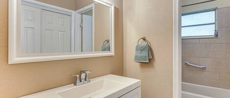 Une salle de bain avec un lavabo blanc, un grand miroir et un espace douche.
