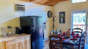 Una cocina con armarios de madera, un refrigerador negro, una mesa de comedor con sillas y una ventana con persianas.