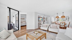 A modern living room with a glass coffee table, white sofas, and a dining area with wicker chairs. - Stunning ocean view condo in Sanibel, 2BR, 2BA, perfect for up to 6 guests. (Sanibel)