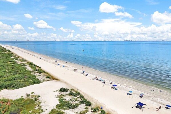 A beach with clear blue water, sandy shore, and umbrellas.