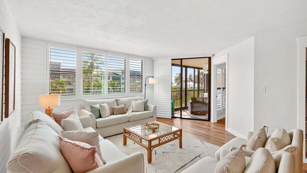 A living room with a sofa, coffee table, and a view through a glass door to an outdoor balcony. - Stunning ocean view condo in Sanibel, 2BR, 2BA, perfect for up to 6 guests. (Sanibel)