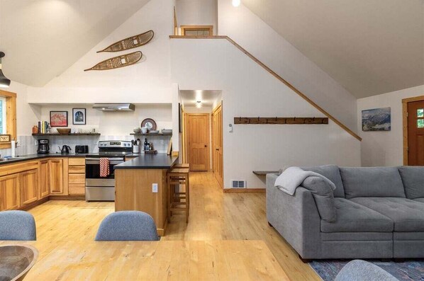 Una cocina moderna con armarios de madera, una isla central y un sofá gris en la sala de estar.