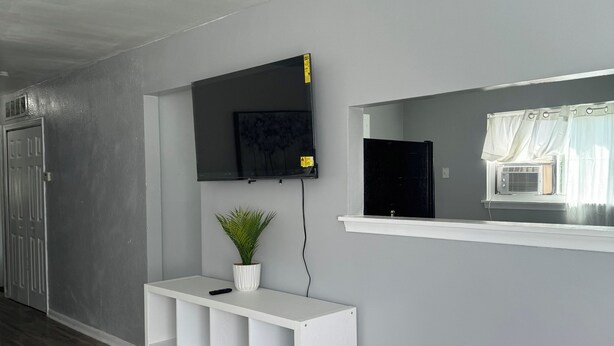 A modern living room with a grey wall, a mounted TV, a white console table with a plant, and a window with curtains.
