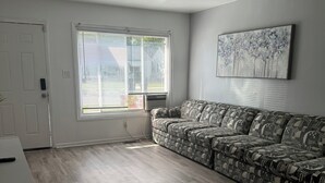 A living room with a patterned sofa, a white door, and a window with blinds.