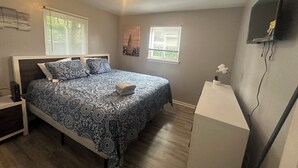 A bedroom with a bed, two windows, a nightstand, a dresser, and a wall-mounted TV.
