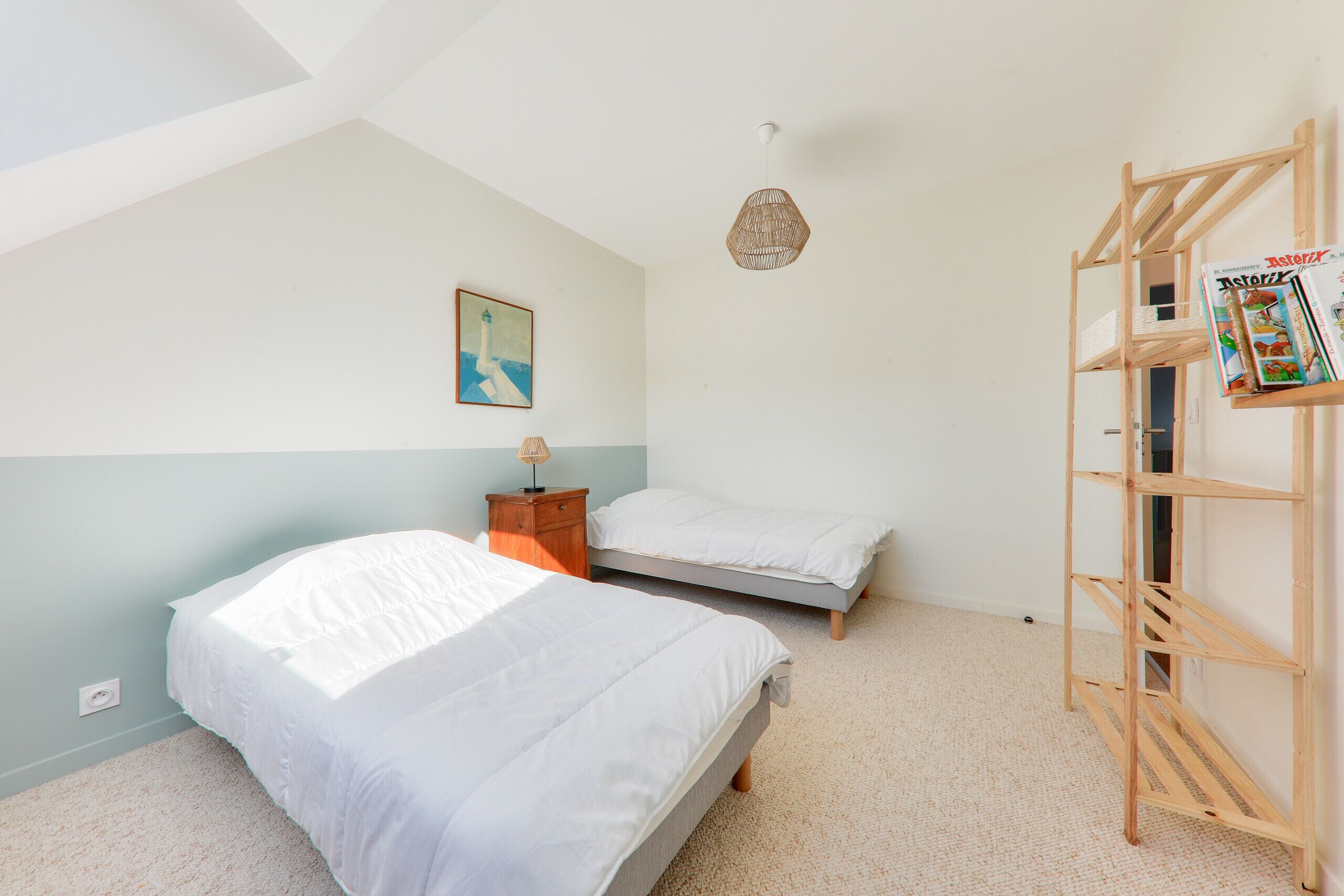 A bedroom with two beds, a wooden ladder, a painting on the wall, and a ceiling light.