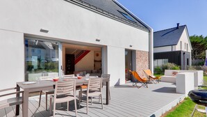 Et moderne udendørs spiseområde med træterrasse, grill og en glasindrammet patio.