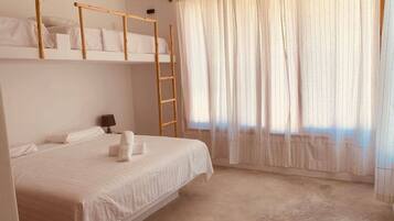 Una cama individual con una escalera de madera, una mesita de noche con lámpara y una ventana con cortinas de encaje.